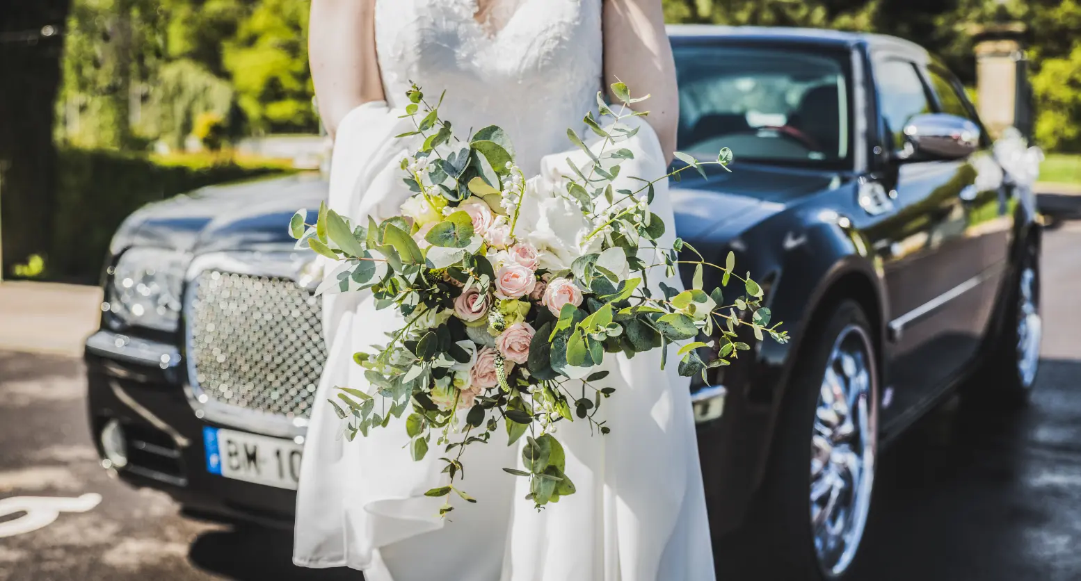 A bride holding her bouquet in front of a chrysler car.