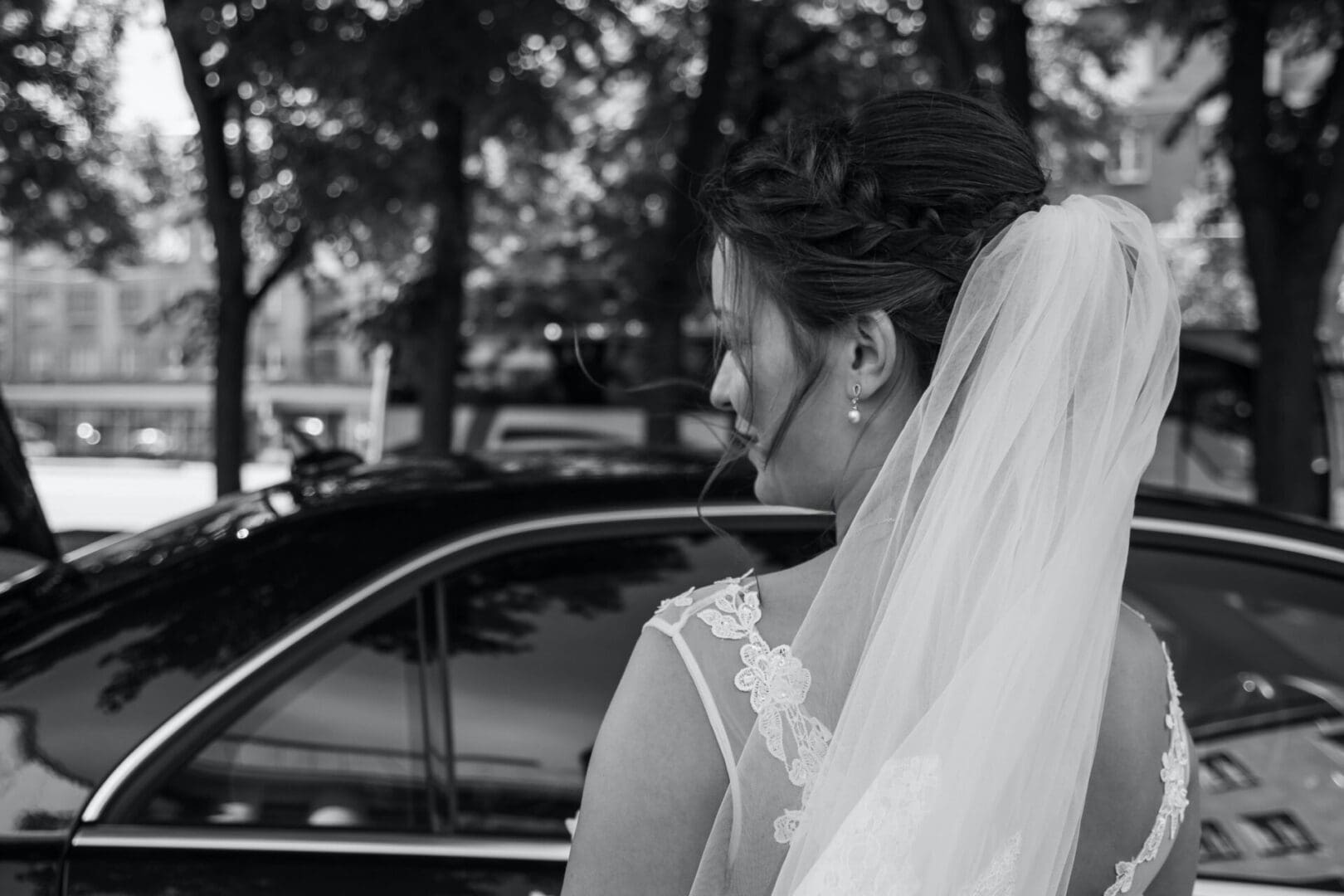 Black and white photo of a bride standing next to her car.