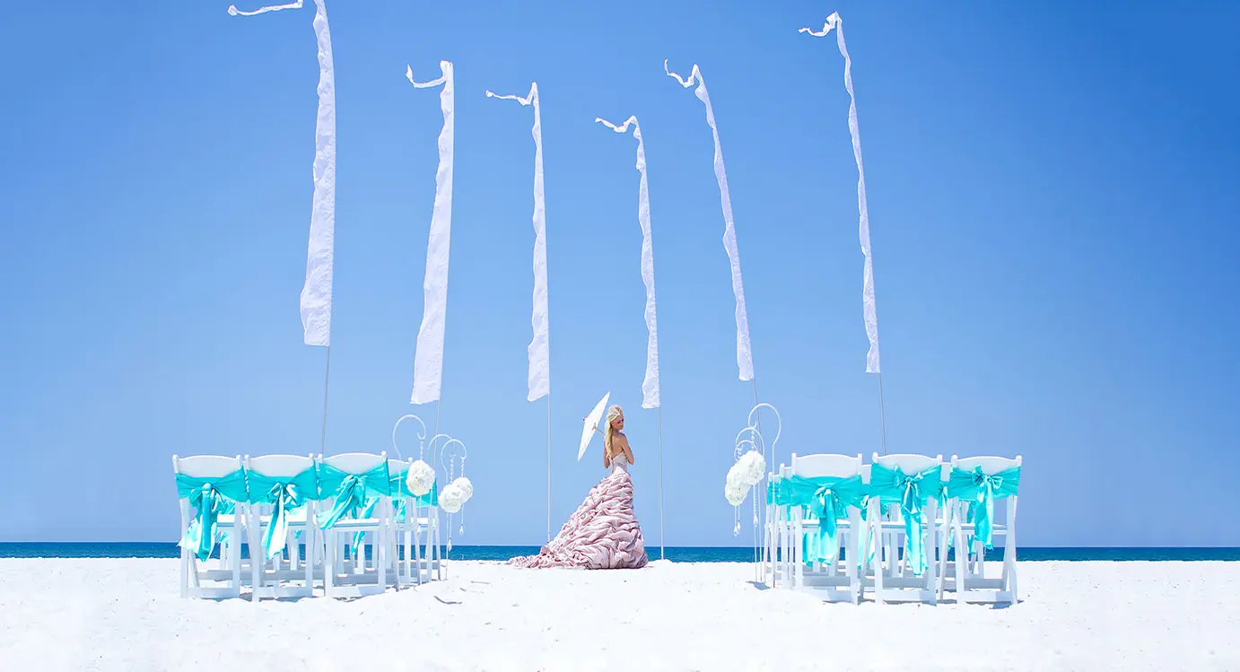 A woman sitting on the beach under some blue umbrellas