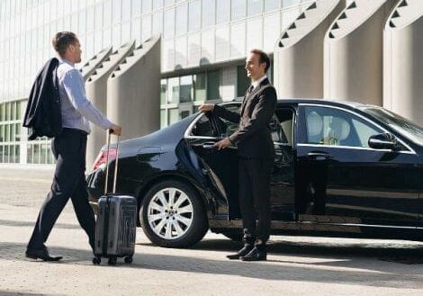 A man in suit and tie pulling luggage from the back of a car.